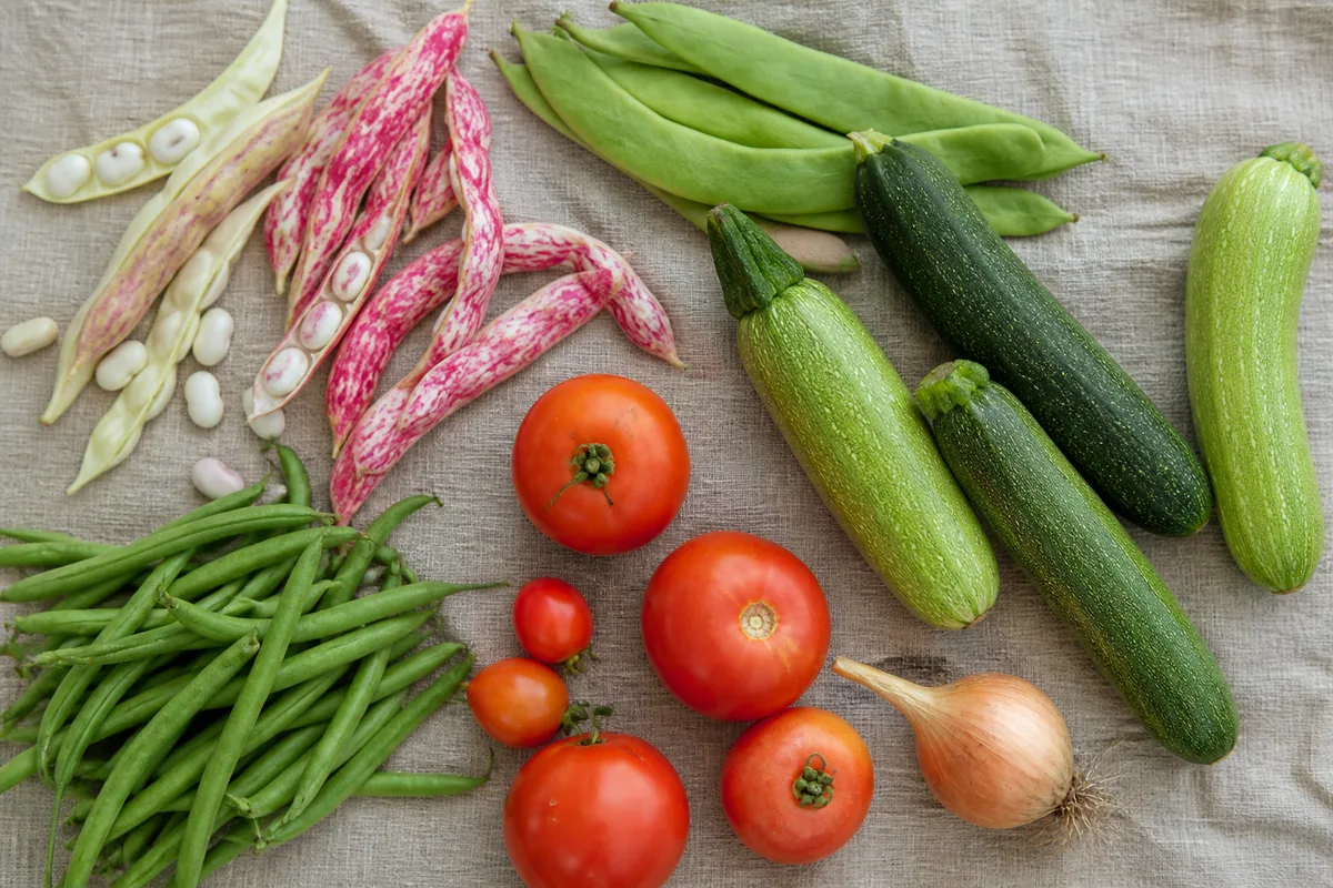 Cocos frais à écosser, haricots verts plats et courgettes posés sur une table de cuisine